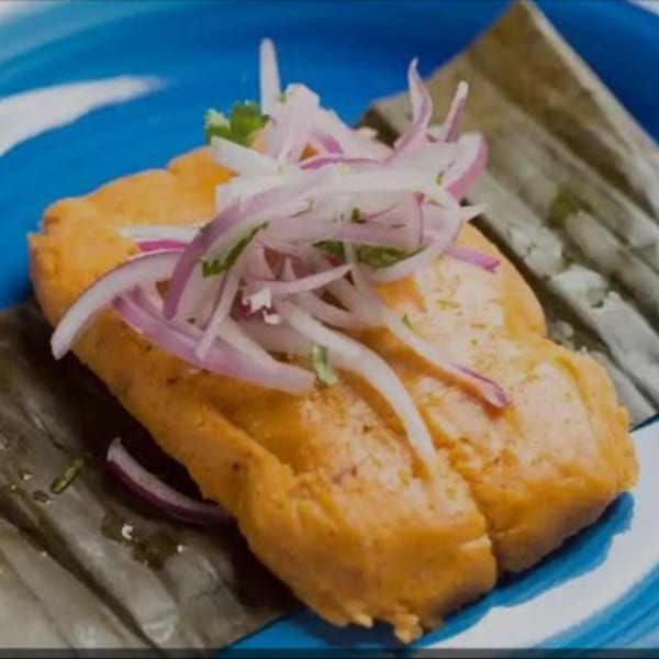Peruvian tamale topped with red onion and cilantro, served on a blue and white plate.