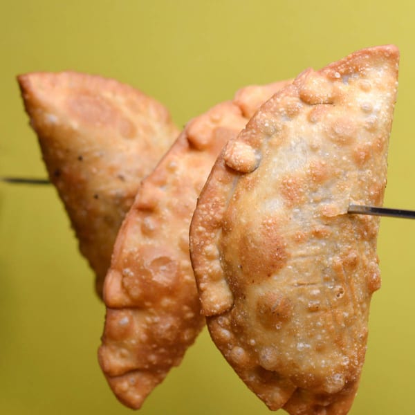 Three golden-brown Peruvian empanadas, deep-fried and crispy, skewered against a vibrant yellow background.
